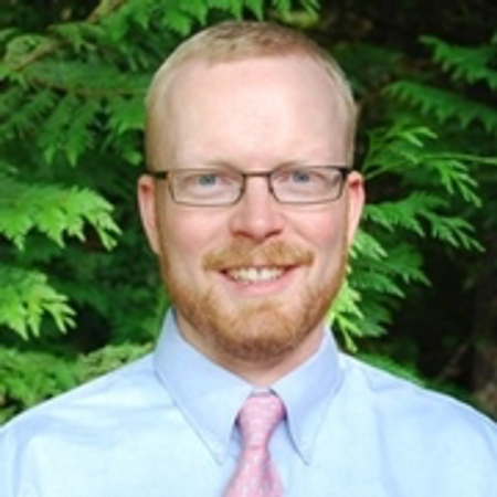 Professional headshot of Jay Zarnetske in a blue button up shirt in front of trees