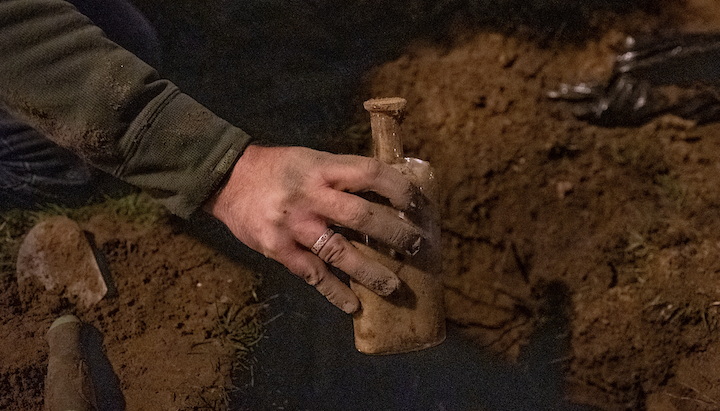 Hand lifts a glass bottle dug from the earth on the MSU campus