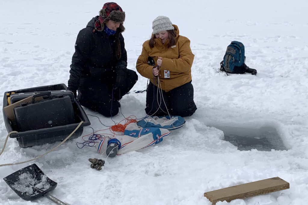 2 women assemble research equipment on lake ice